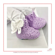 Image is a baby doll wearing crochet booties with african fabric on the sole.